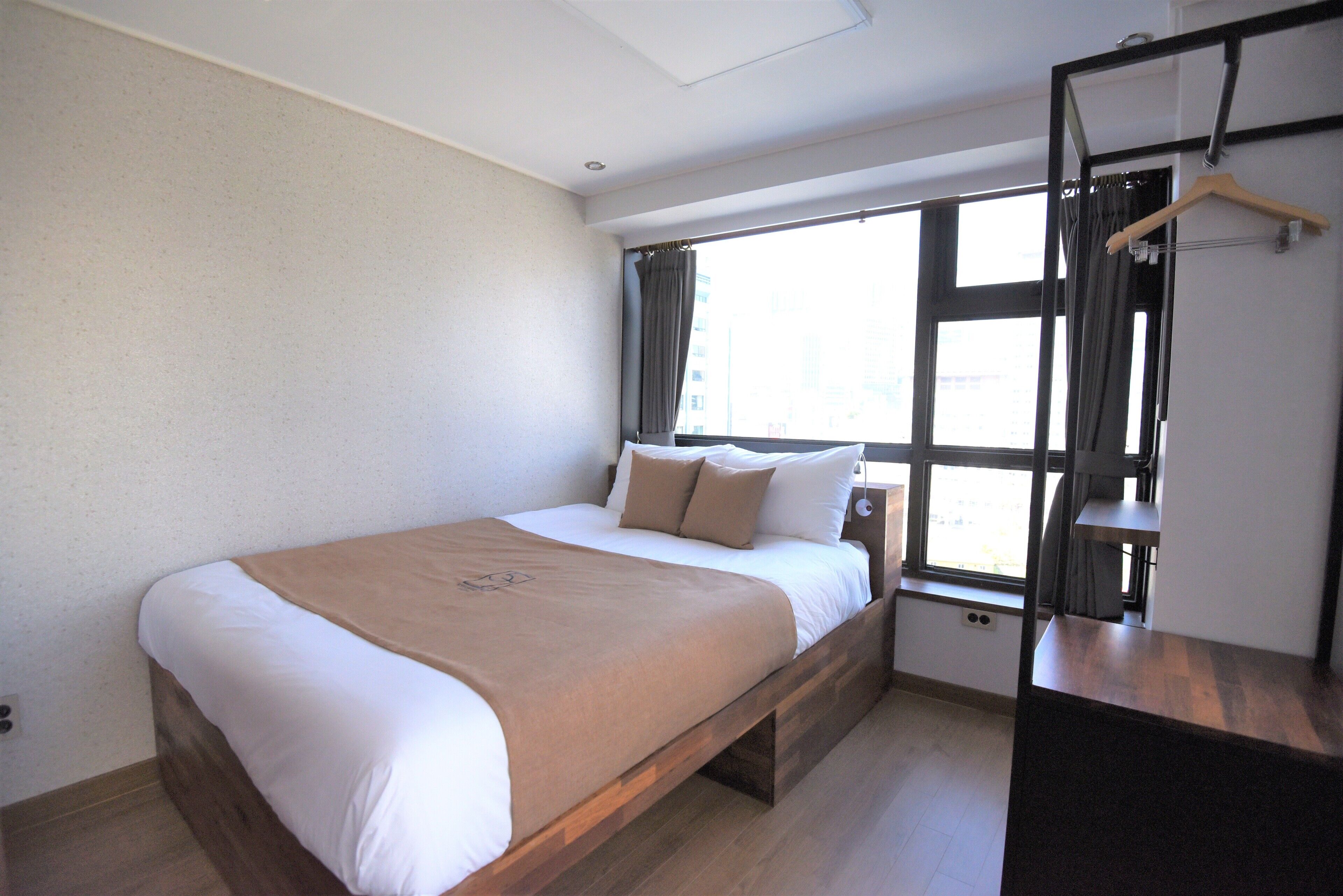 A modern bedroom with a large bed, a wooden headboard, a bedside table, and a window with curtains.