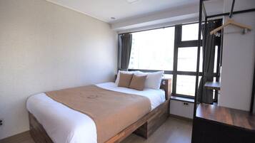 A modern bedroom with a large bed, a wooden headboard, a bedside table, and a window with curtains.