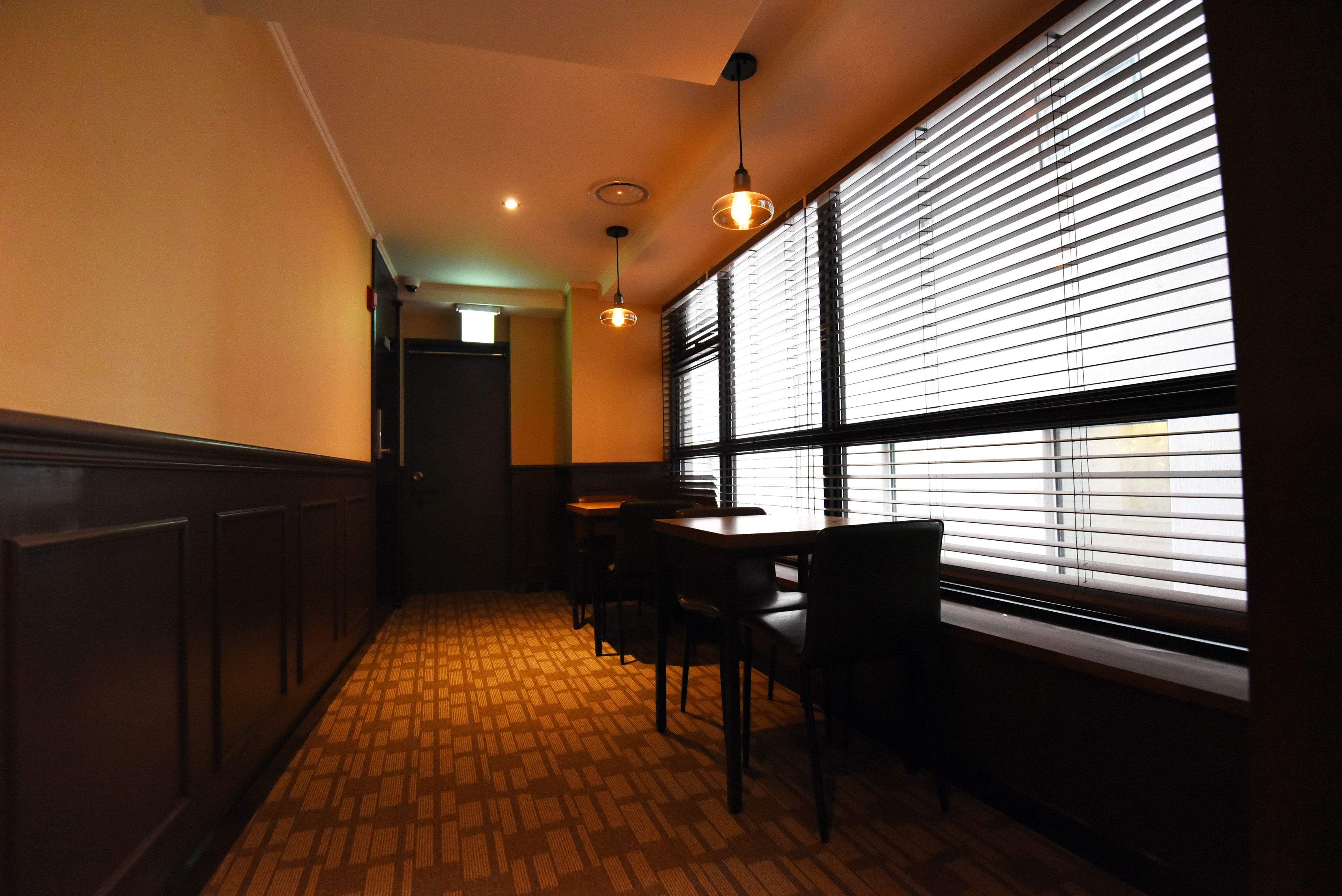 A narrow hallway with patterned flooring, a table with chairs, and a window with blinds.