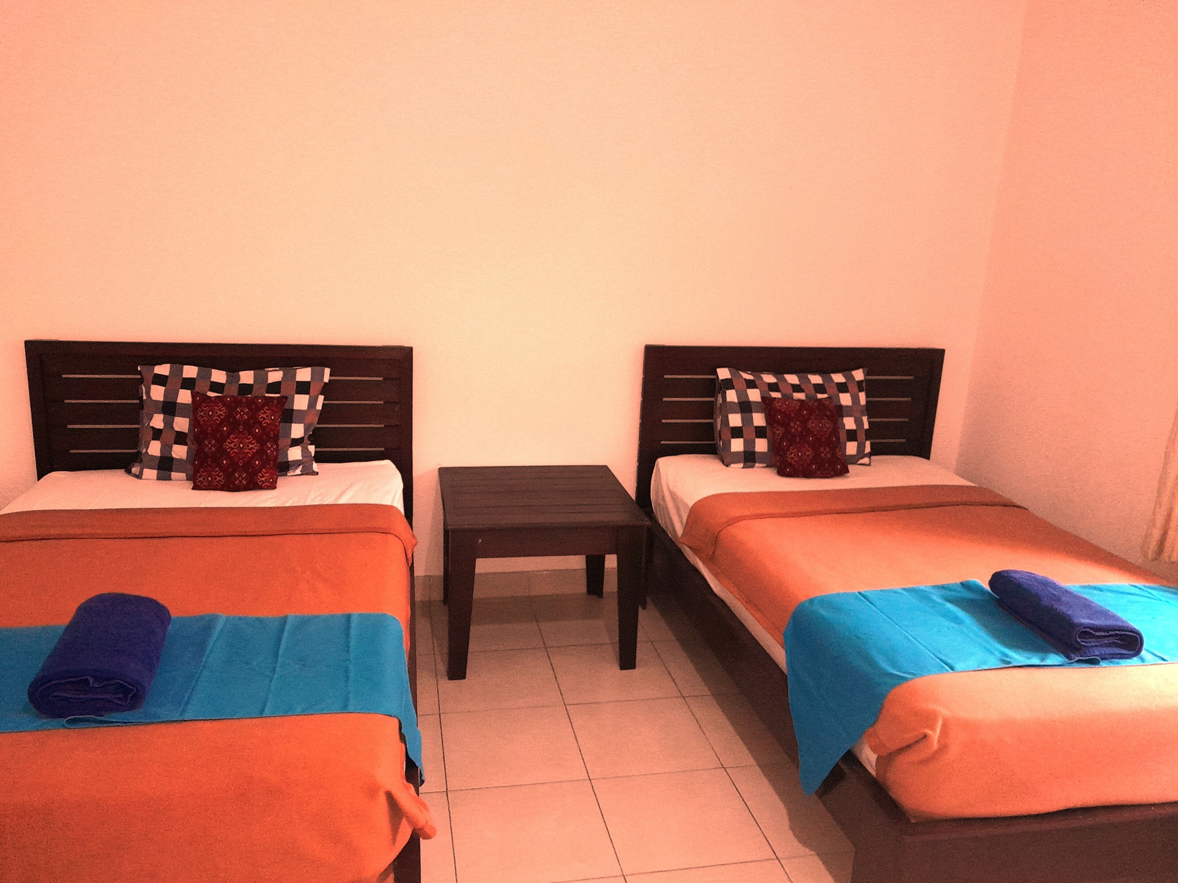 Two single beds with wooden headboards, a small table, and a tiled floor.