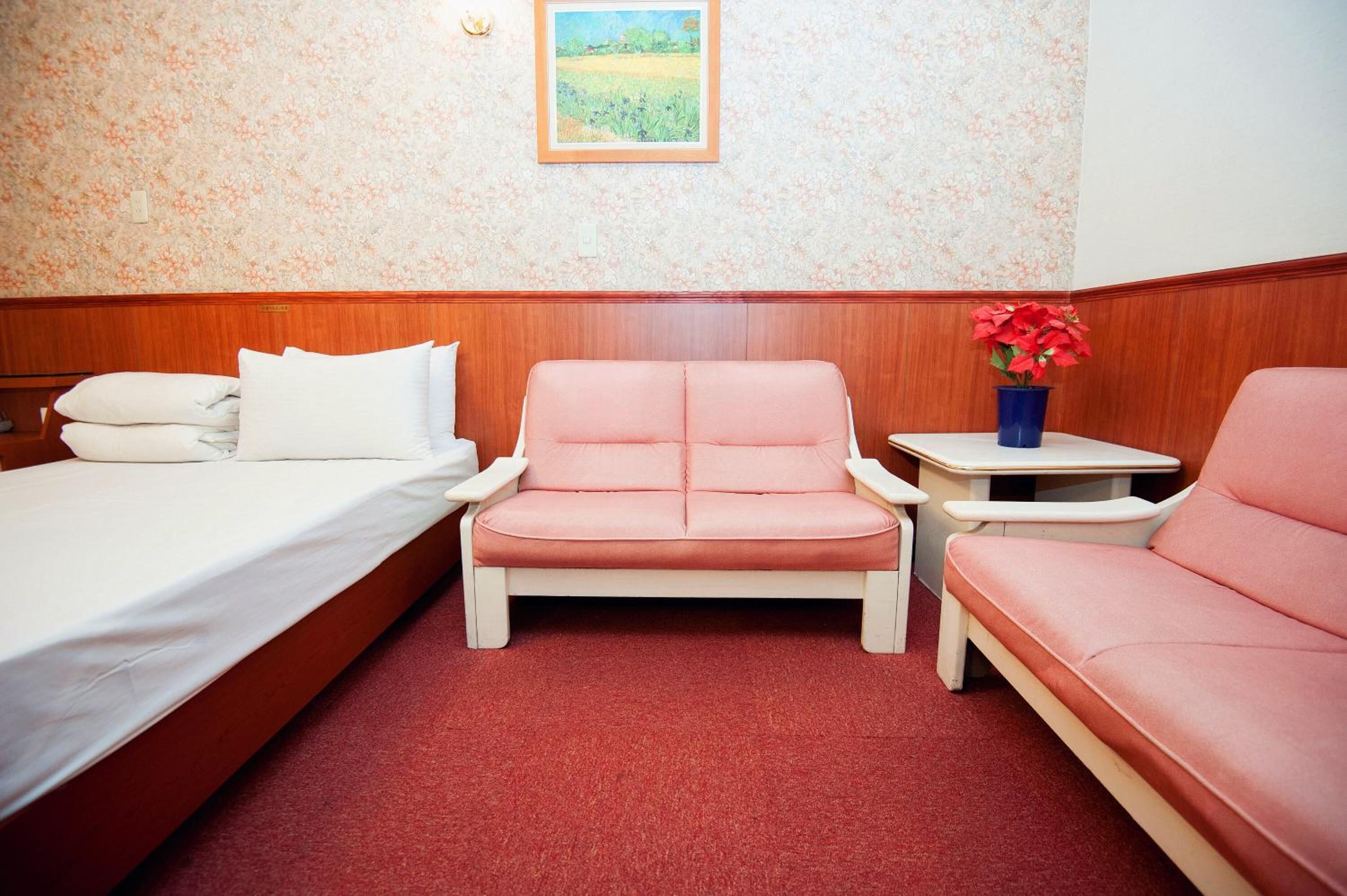 A room with a bed, a pink sofa, a small table with a vase of flowers, and a wall with a floral pattern.