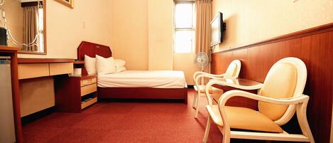 A hotel room with a bed, a desk with a chair, a mirror, a TV, and a window with curtains.