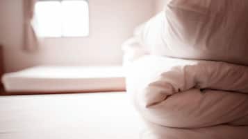 A bed with white bedding and pillows, a window with blinds, and a wooden floor.