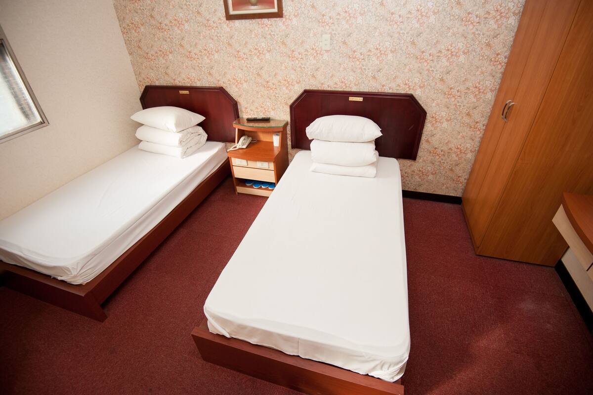 Two single beds with wooden headboards, a small bedside table with a phone and a lamp, and a wooden wardrobe.
