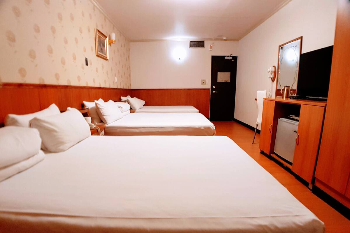 A hotel room with two beds, a wooden wardrobe, a television, and a door.