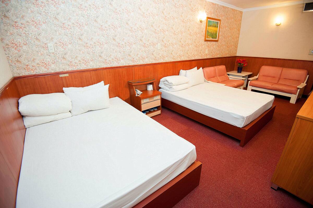 A hotel room with two beds, a small table with a vase of flowers, and a wooden cabinet.