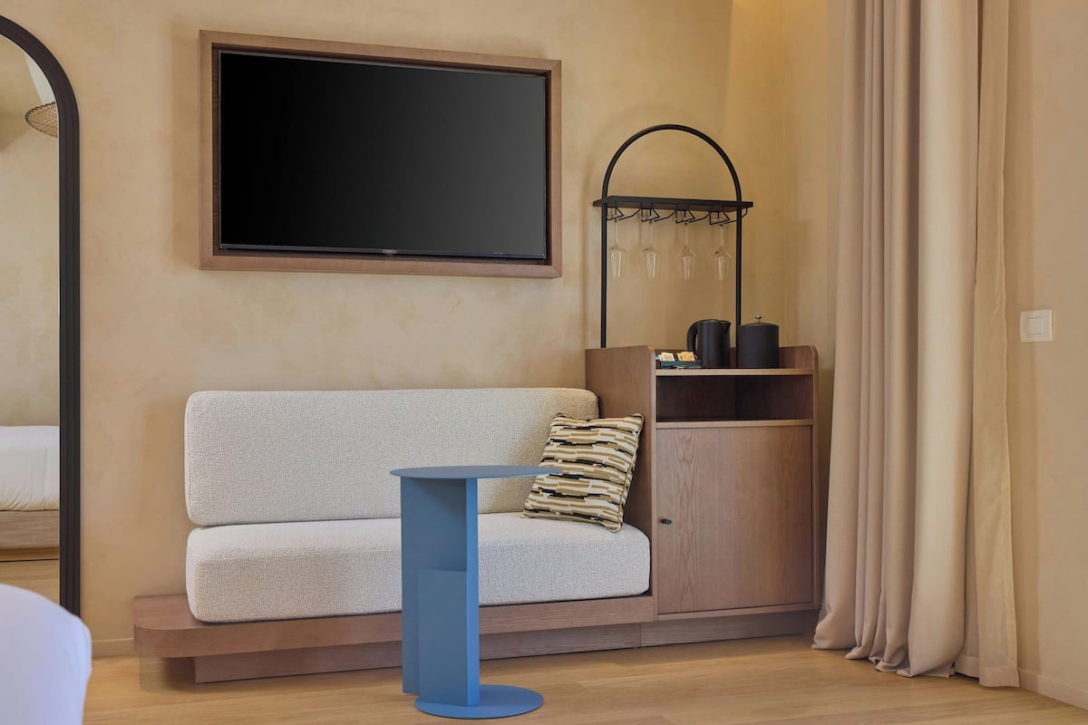 Ein modernes Zimmer mit einer Couch, einem kleinen blauen Tisch, einem an der Wand montierten Fernseher, einem Schrank und einem Vorhang.