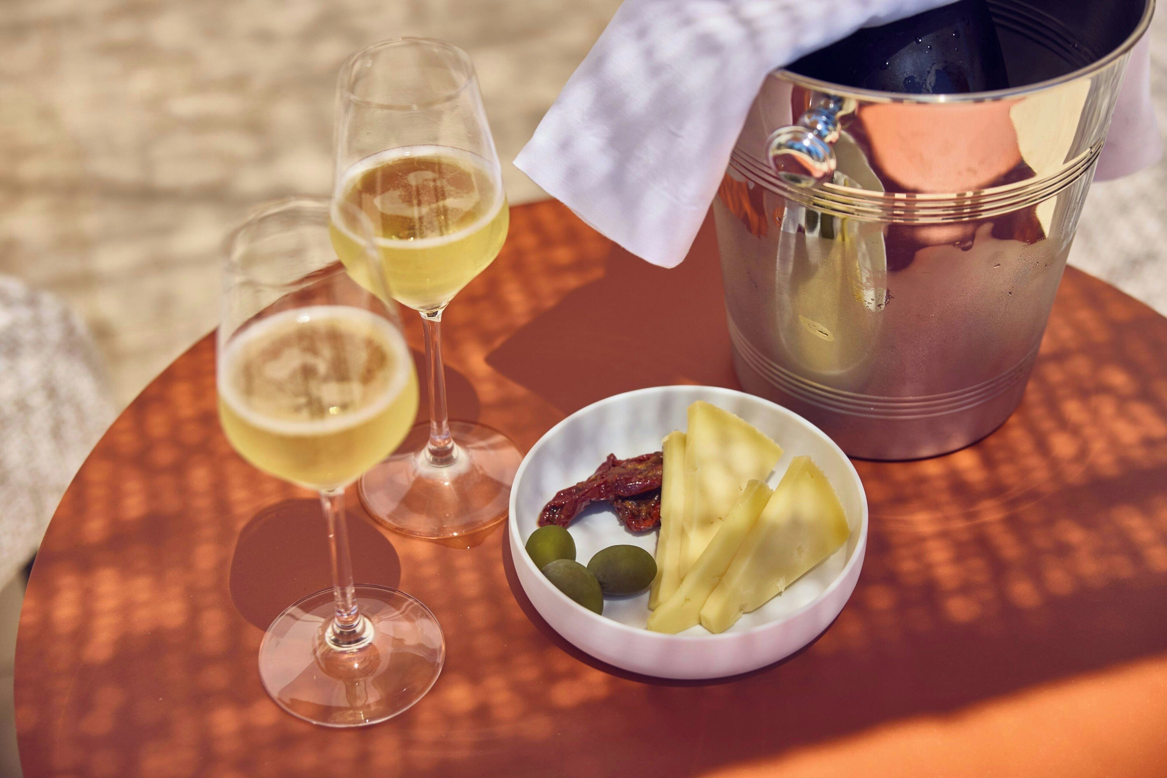 A table with two glasses of a light-colored beverage, a bowl of fruit, and a metal container.