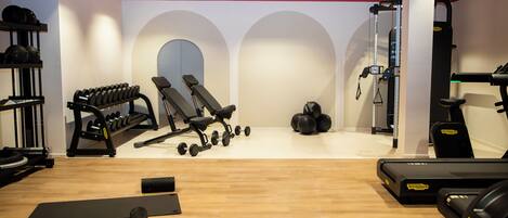 Un gimnasio con equipo de ejercicio, incluyendo mancuernas, una banca y cintas de correr.