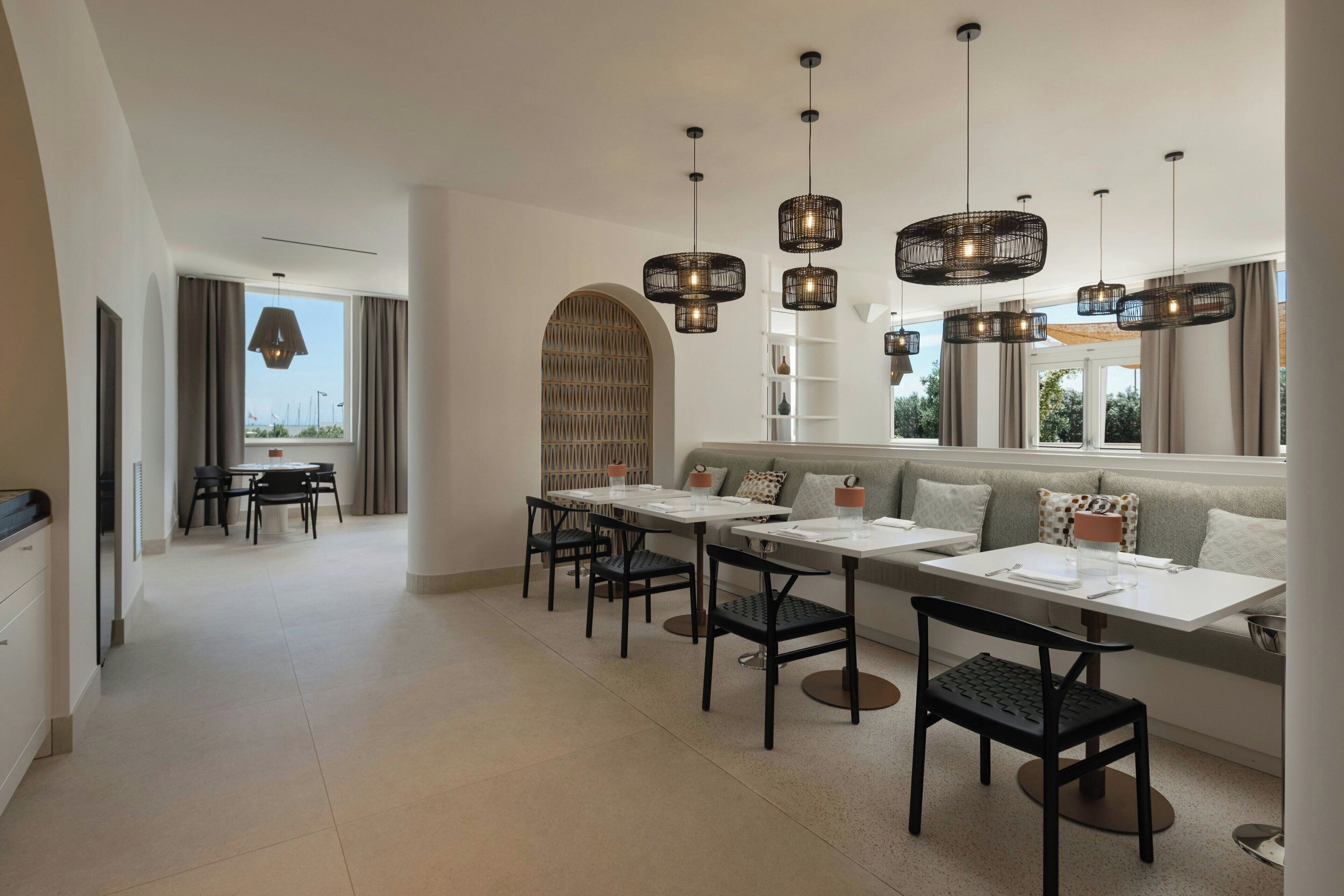 Un espace de restauration moderne avec une longue table, de nombreuses chaises et des luminaires suspendus.