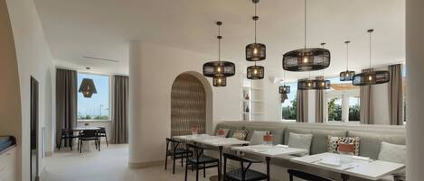A modern dining area with a long table, multiple chairs, and hanging pendant lights.