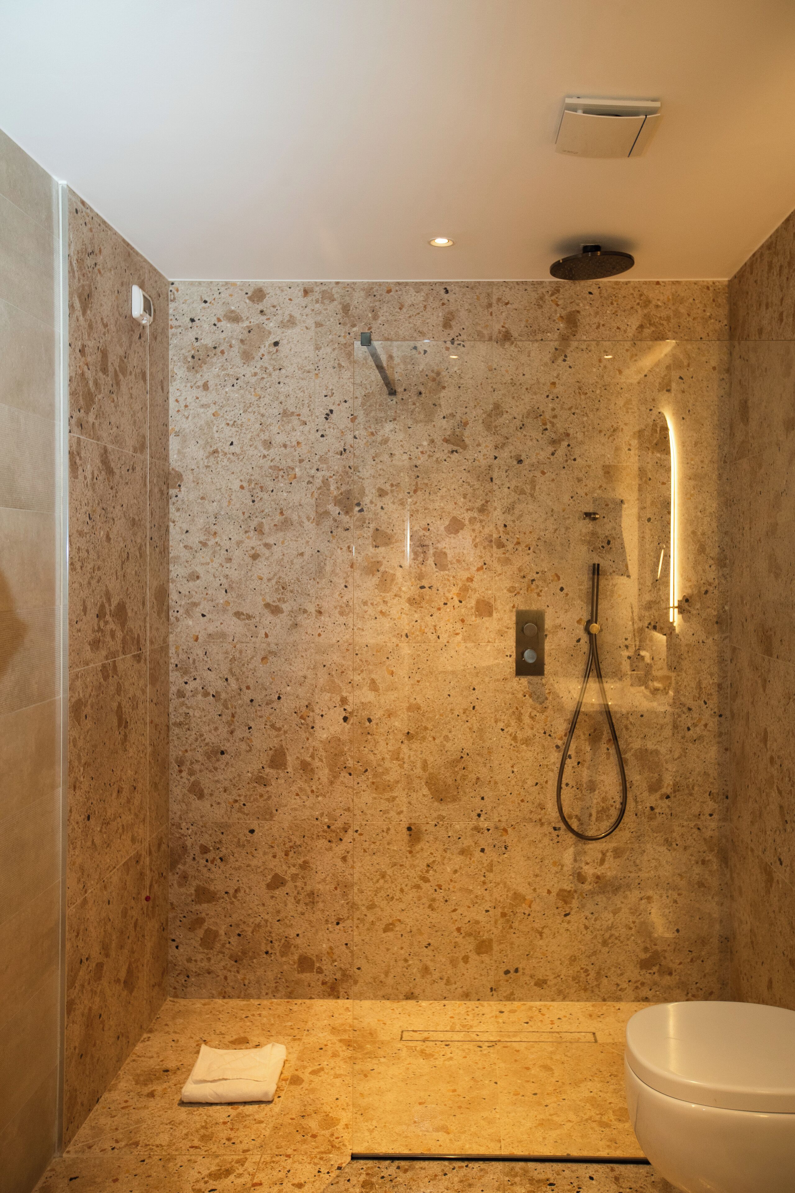 A bathroom with a shower, a toilet, and a towel on the floor.