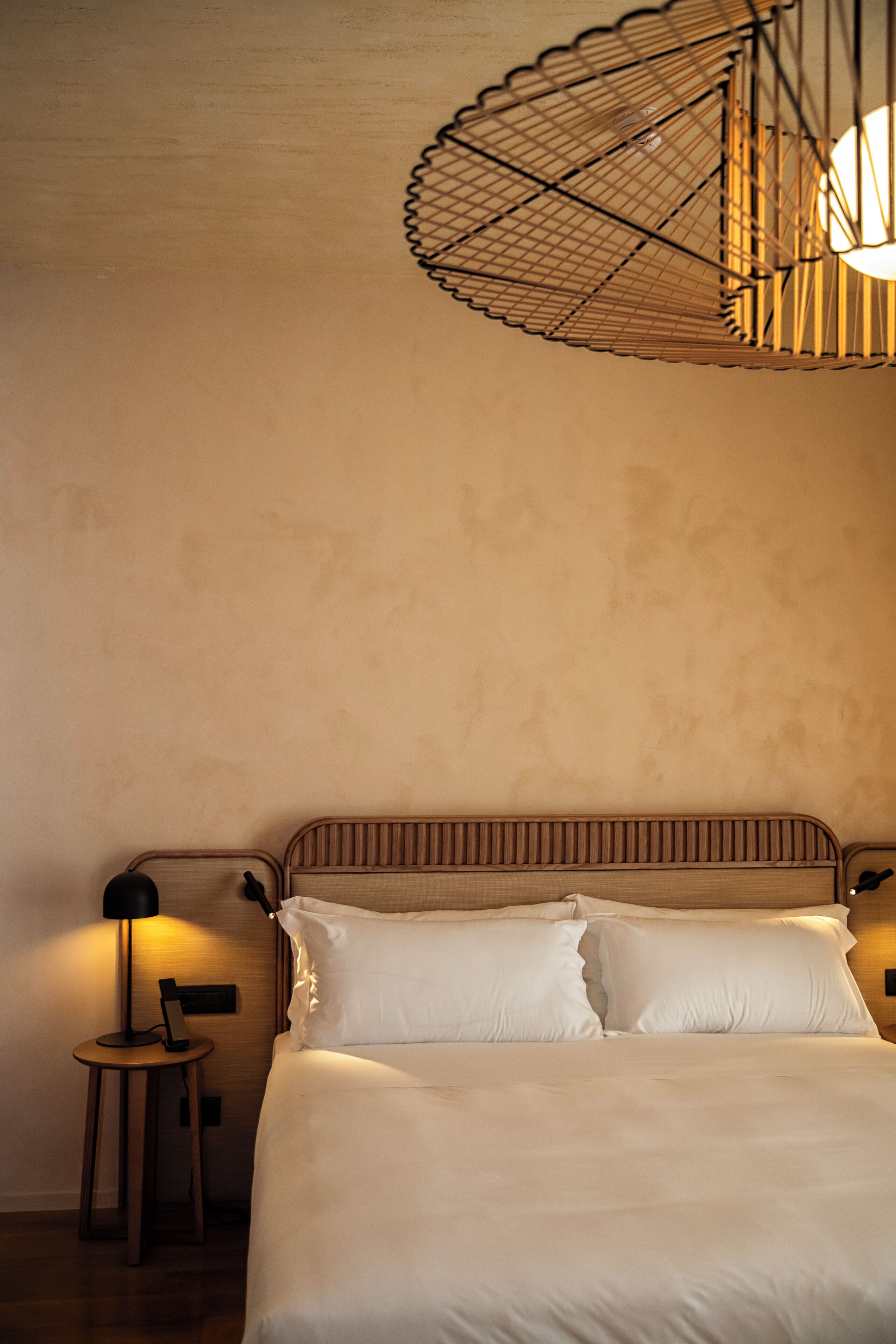 A neatly made bed with white linens, a wooden headboard, and a small bedside table with a lamp.