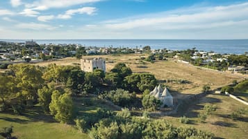 Vista aerea di una cittadina costiera con un'imponente struttura simile a un castello, circondata dal verde e con una chiara vista sul mare.