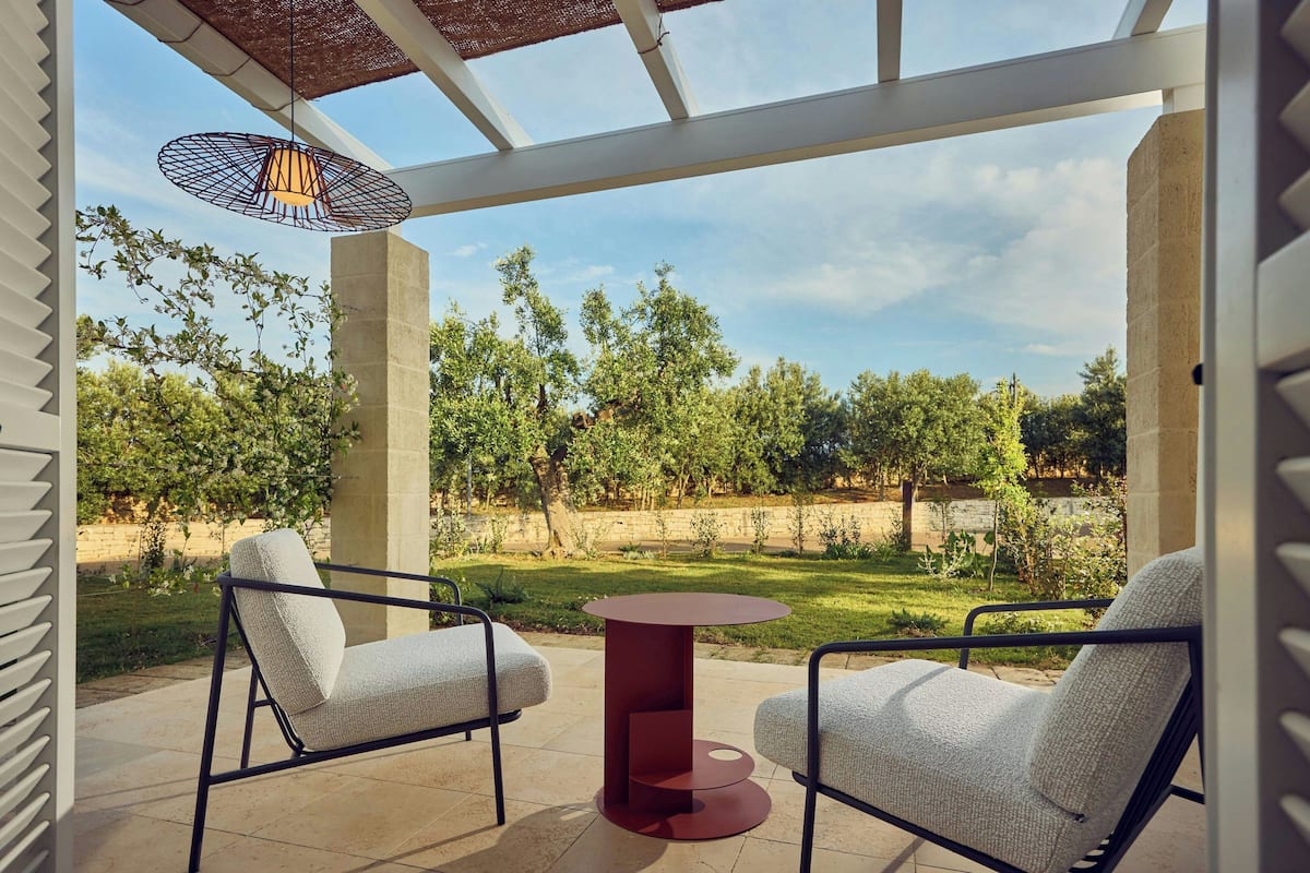 Eine Terrassengruppe im Freien mit zwei weißen Polsterstühlen und einem runden Tisch, umgeben von einem Pergola mit einer hängenden Lampe.