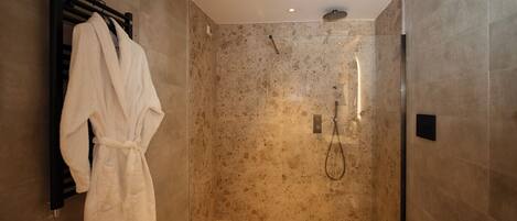A modern bathroom with a walk-in shower, a toilet, and a robe hanging on a rack.
