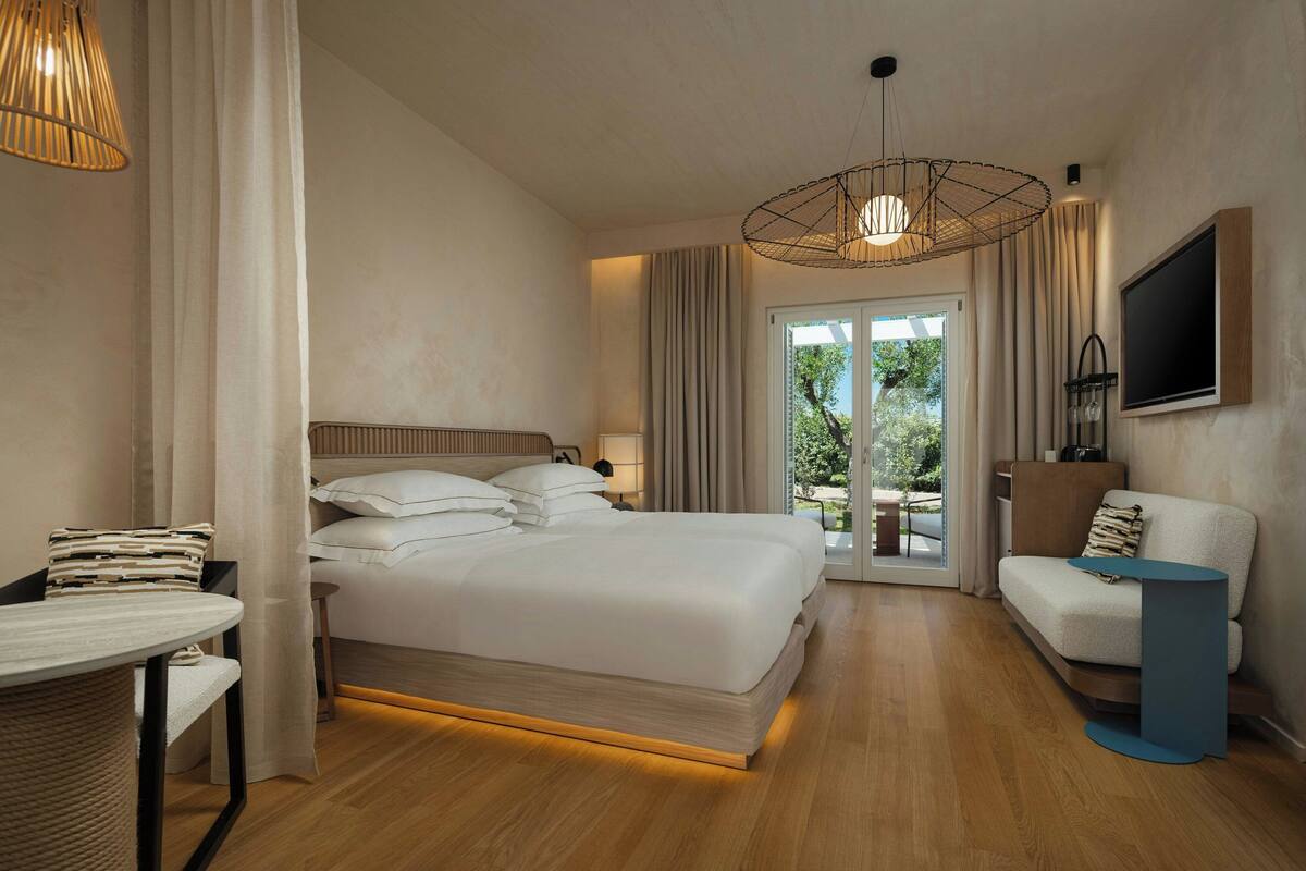 Ein modernes Hotelzimmer mit einem großen Bett, einer Sitzecke, einem Fernseher und Blick ins Freie.