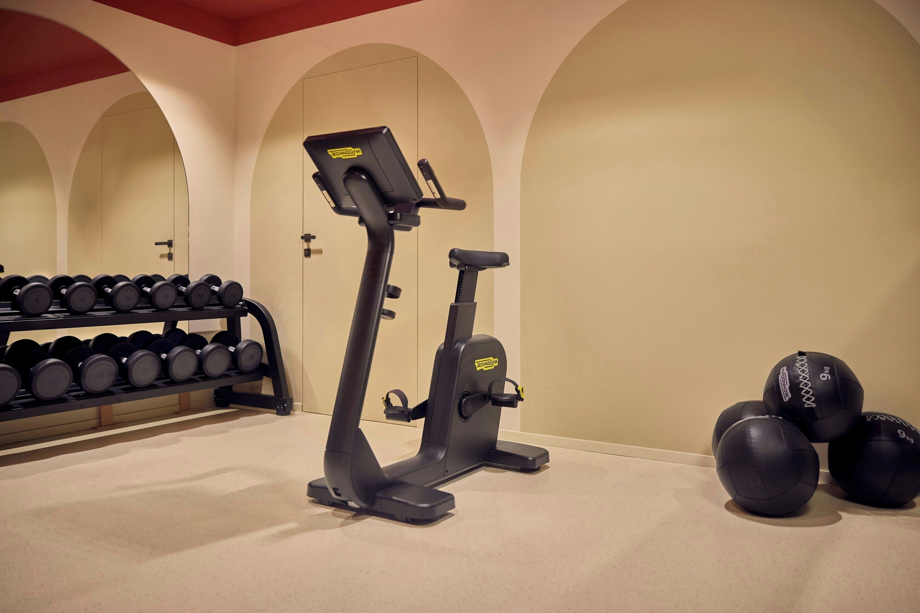 Een fitnessruimte met trainingsapparatuur, een dumbbellsrek en trainingsballen.
