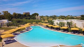A swimming pool with sun loungers and umbrellas, surrounded by greenery and buildings. - Cala Ponte, a Tribute Portfolio Hotel (Polignano a Mare)