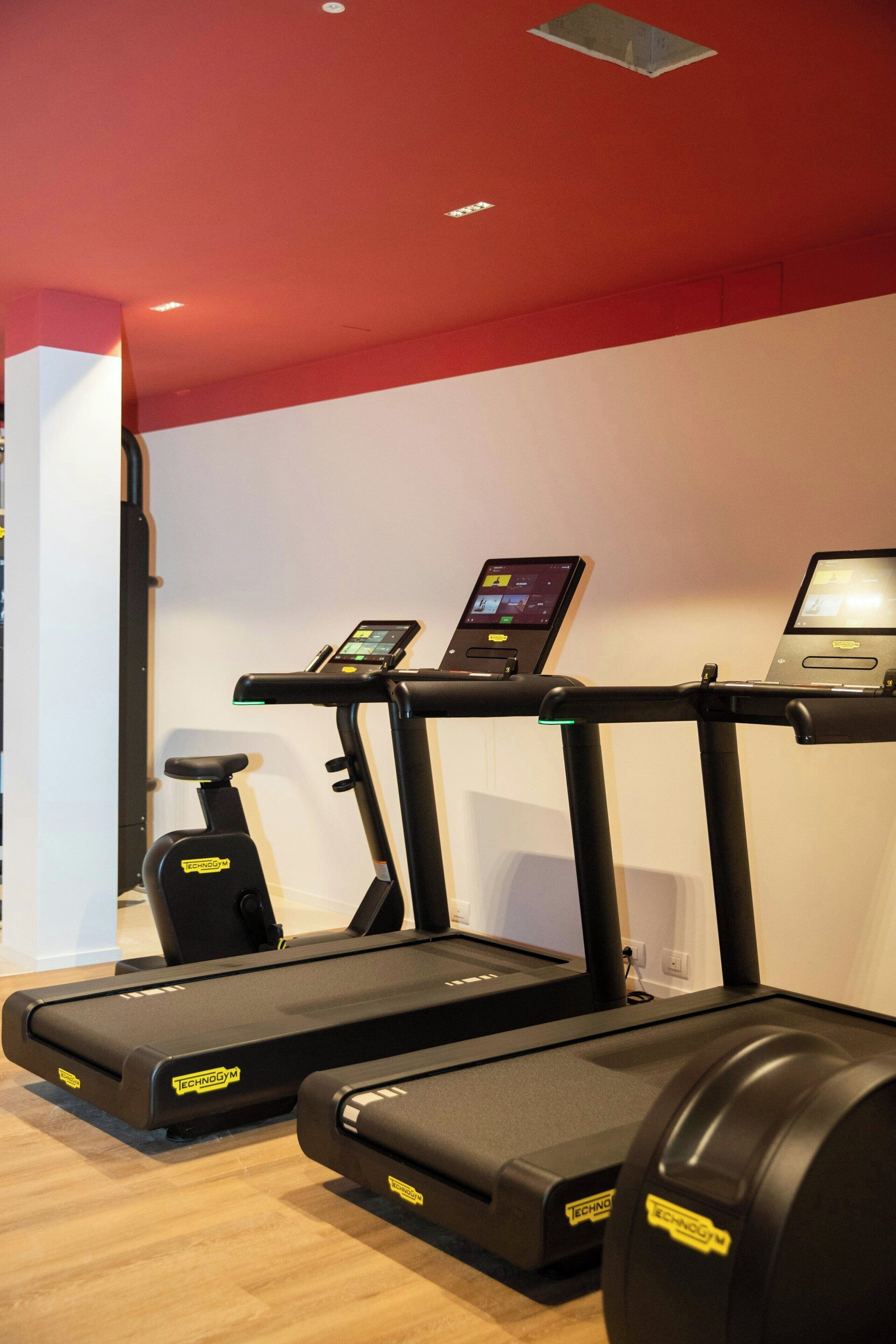 A gym with two treadmills, one with a digital display and a laptop on top, and a stationary bike.