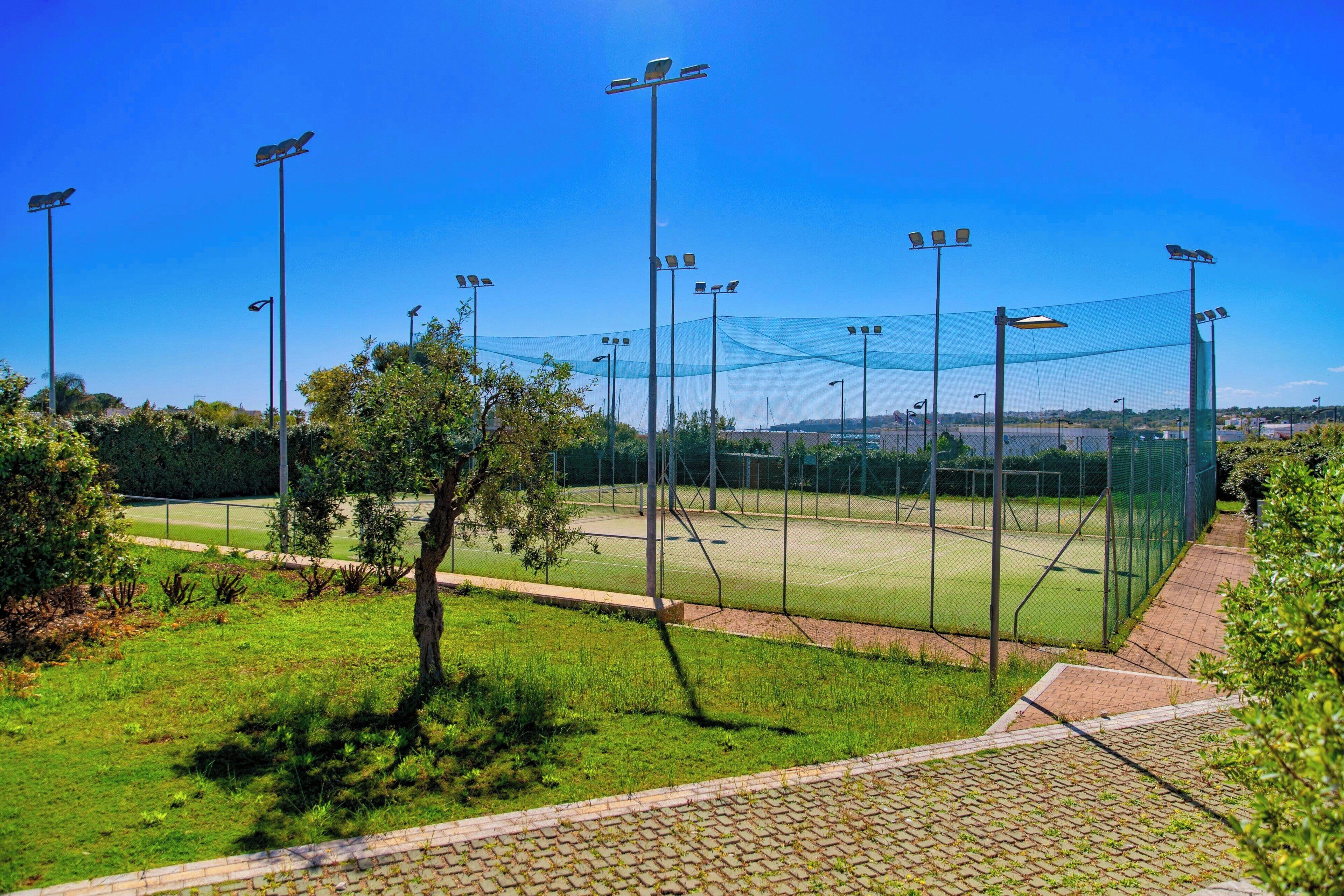 A tennis court with a net, surrounded by trees and a brick pathway.