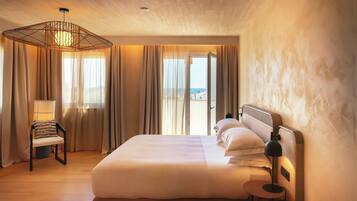 Habitación de hotel con una cama grande, una silla, un escritorio y vistas al mar.