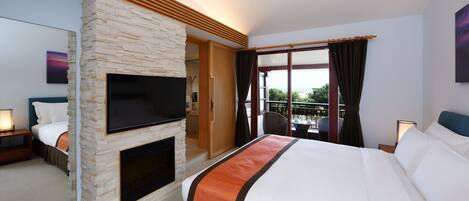A hotel room with a stone fireplace, a flat-screen TV, a large bed, and a balcony with a view.