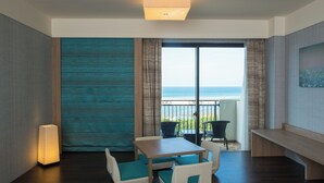 Een kamer met een houten tafel, witte gestoffeerde stoelen, een bankje en uitzicht op de zee door een groot raam.