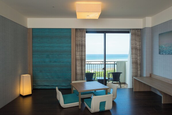 A room with a wooden table, white cushioned chairs, a bench, and a view of the sea through a large window.
