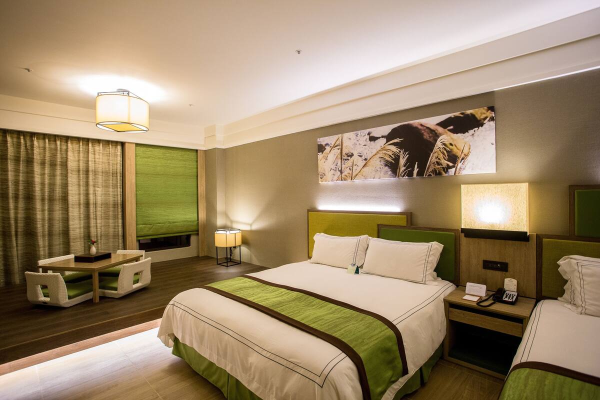 Une chambre d’hôtel comprenant un lit, des tables de chevet, un bureau avec des chaises, une lampe et un tableau au mur.