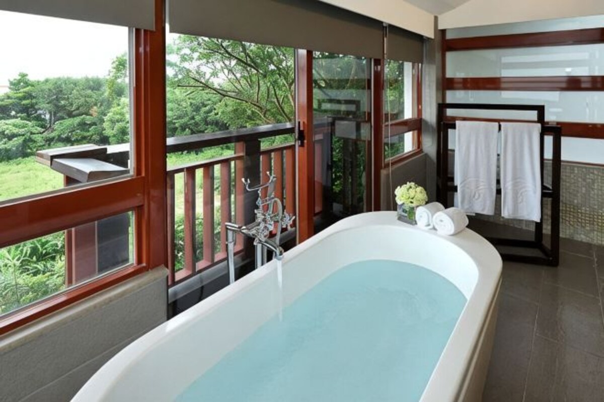 Une salle de bain dotée d’une grande baignoire, d’une douche séparée par des parois en verre et offrant une vue sur l’extérieur.