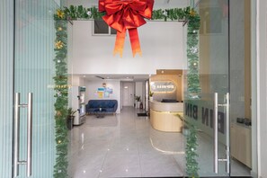 A hotel reception area with a glass door, a reception desk, a blue sofa, and a large red bow decoration.
