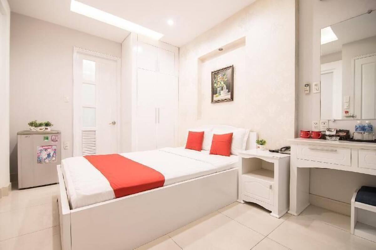 A bedroom with a bed, a desk, a chair, a small fridge, and a mirror.