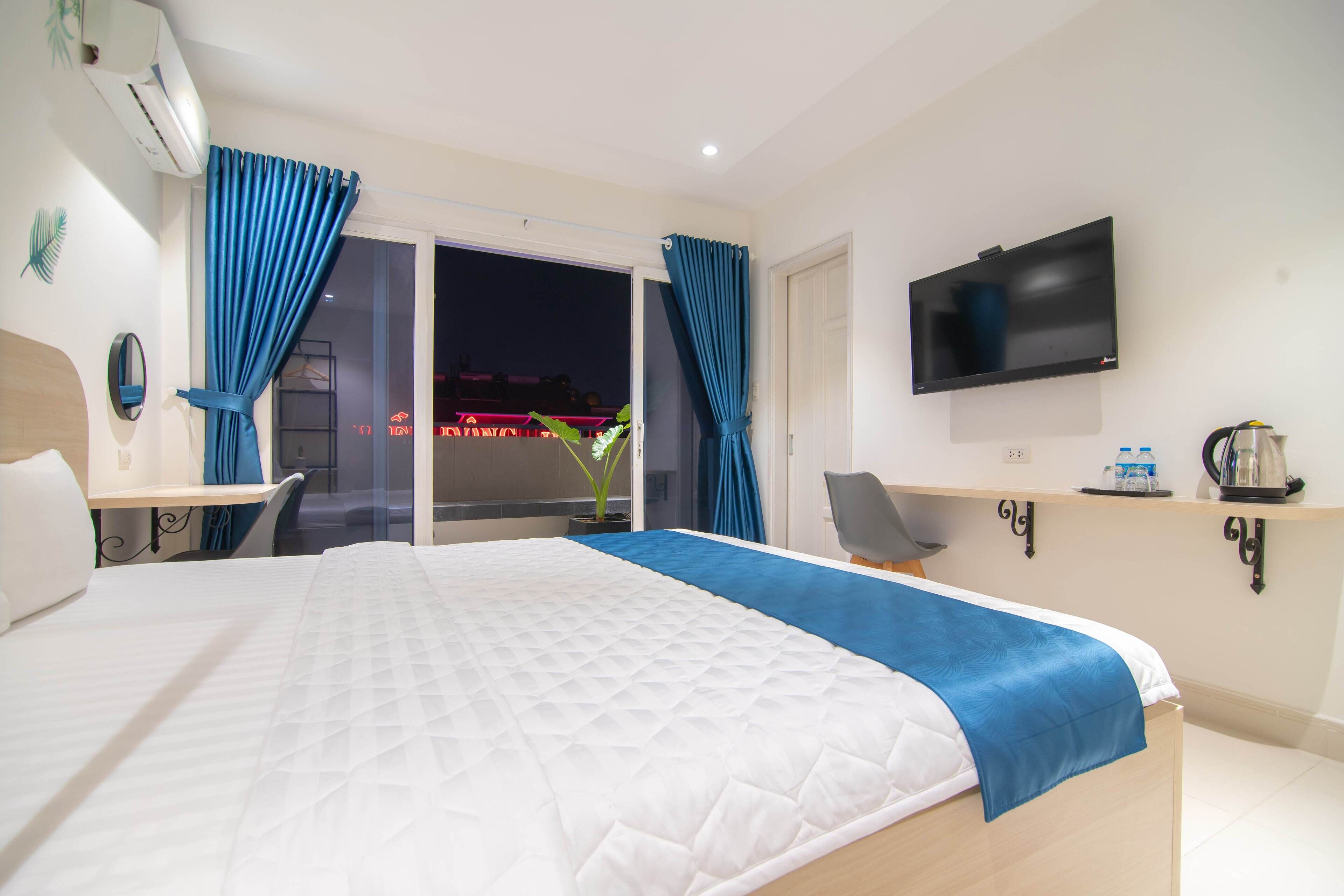 A hotel room with a bed, a desk, a chair, a TV, and a balcony with curtains.