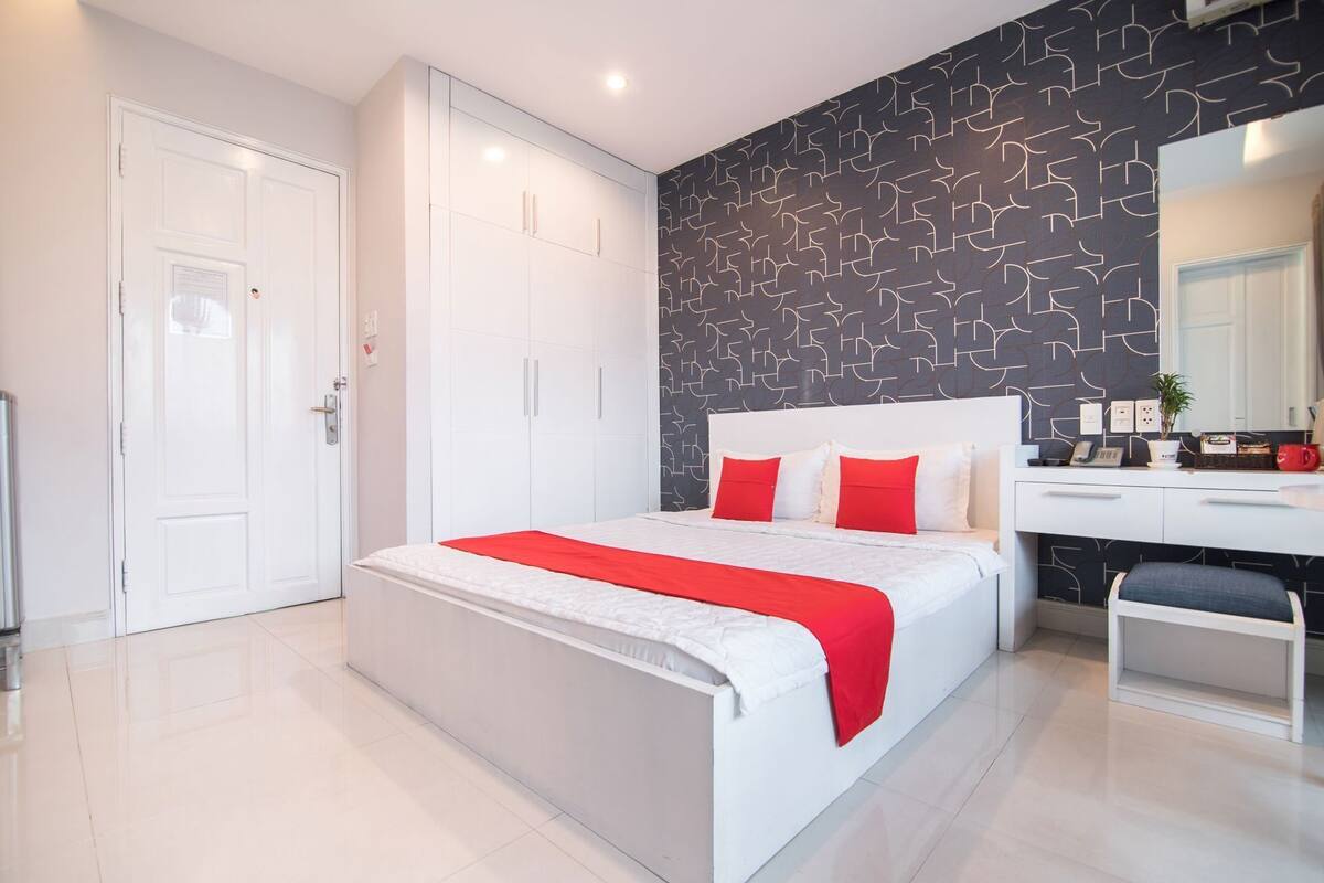 A modern bedroom with a large bed, white wardrobe, and a desk with a chair.