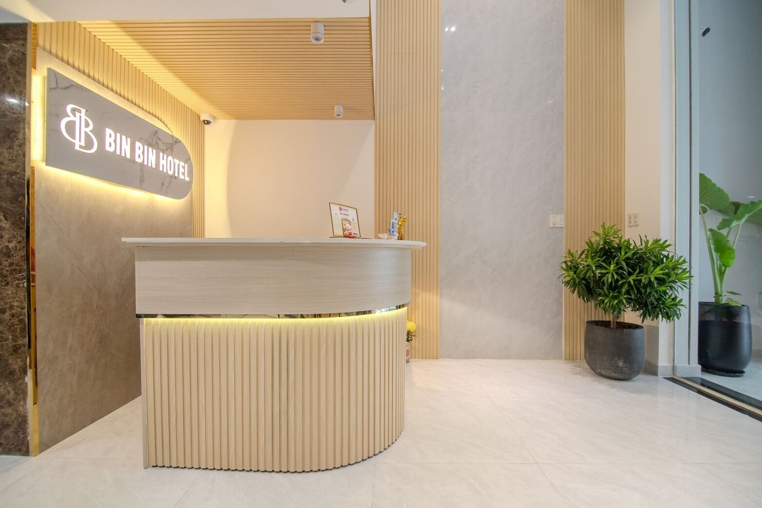 Un mostrador de recepción con un letrero que dice "BIN BIN HOTEL" y una planta en maceta a la derecha.