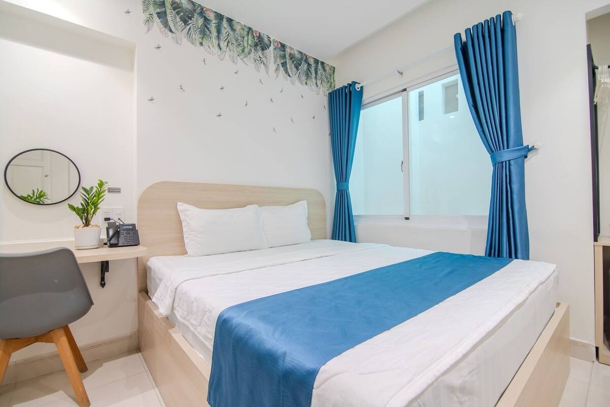 A hotel room with a bed, a desk with a phone, a chair, and a window with curtains.