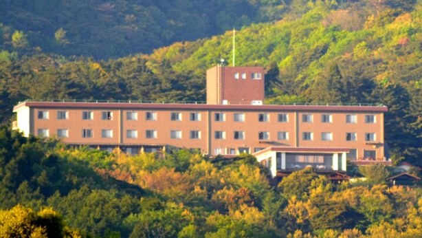A multi-story building with a flat roof, surrounded by dense forest. - Ryokojin Sanso (Kirishima)