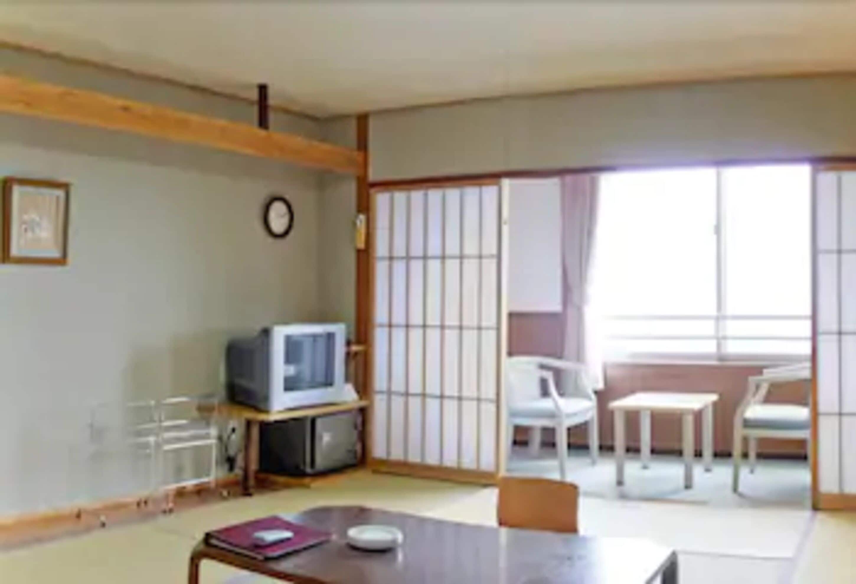 A traditional Japanese-style room with tatami flooring, a low wooden table, a television, sliding shoji doors, and a view of the outside.