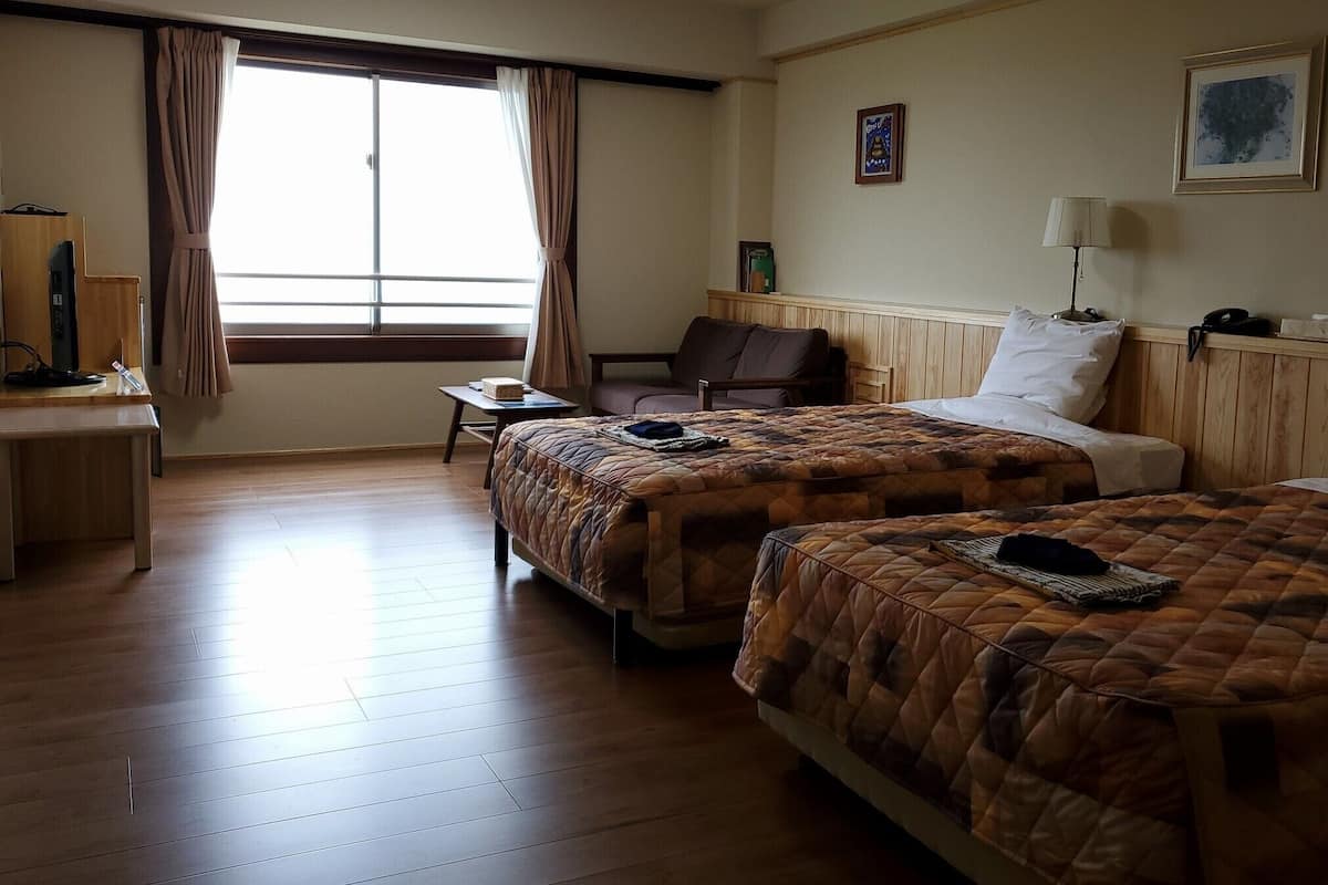 A hotel room with two beds, a desk, a chair, and a window with curtains.