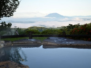A hot spring with a wooden fence, a person in the background, and a mountain in the distance. - Ryokojin Sanso (Kirishima)