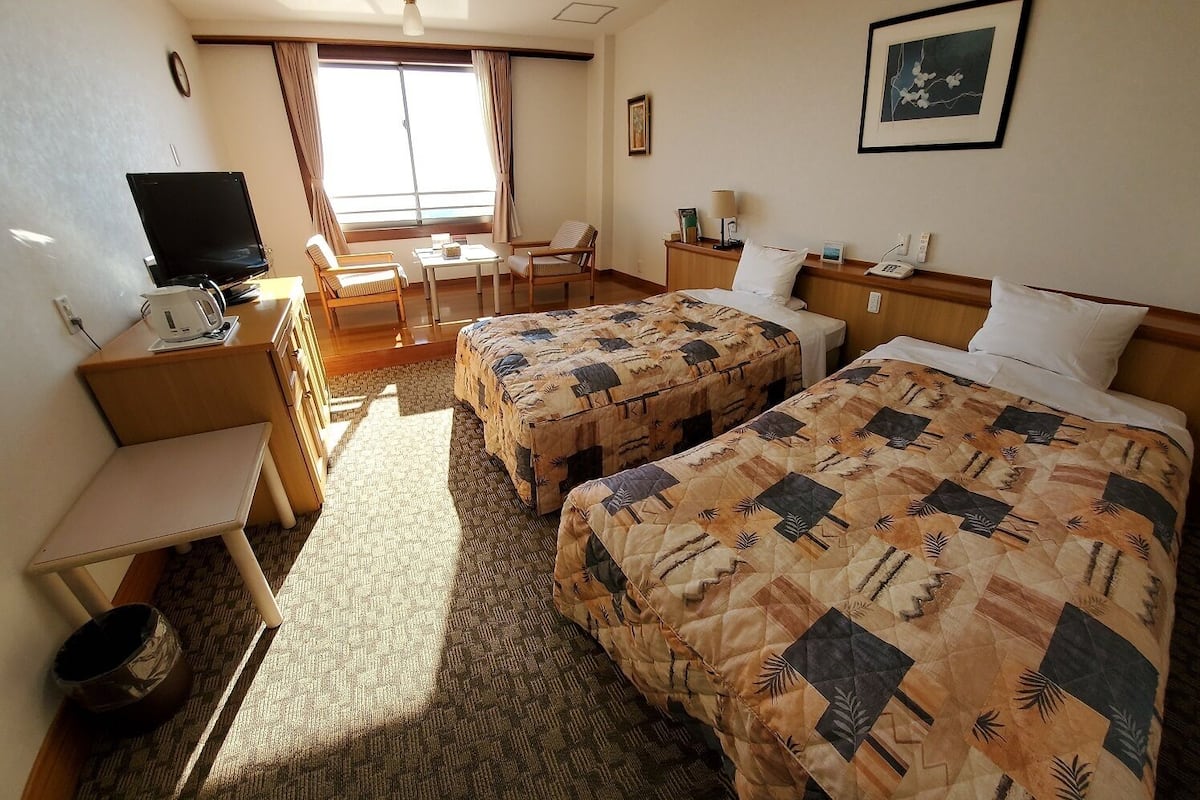 A hotel room with two beds, a desk, a chair, a television, and a window with curtains.