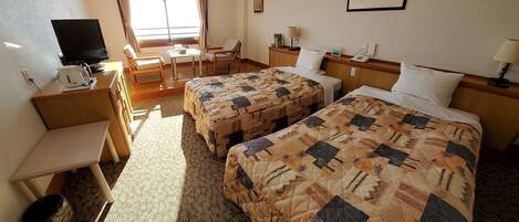A hotel room with two beds, a desk, a chair, a television, and a window with curtains.