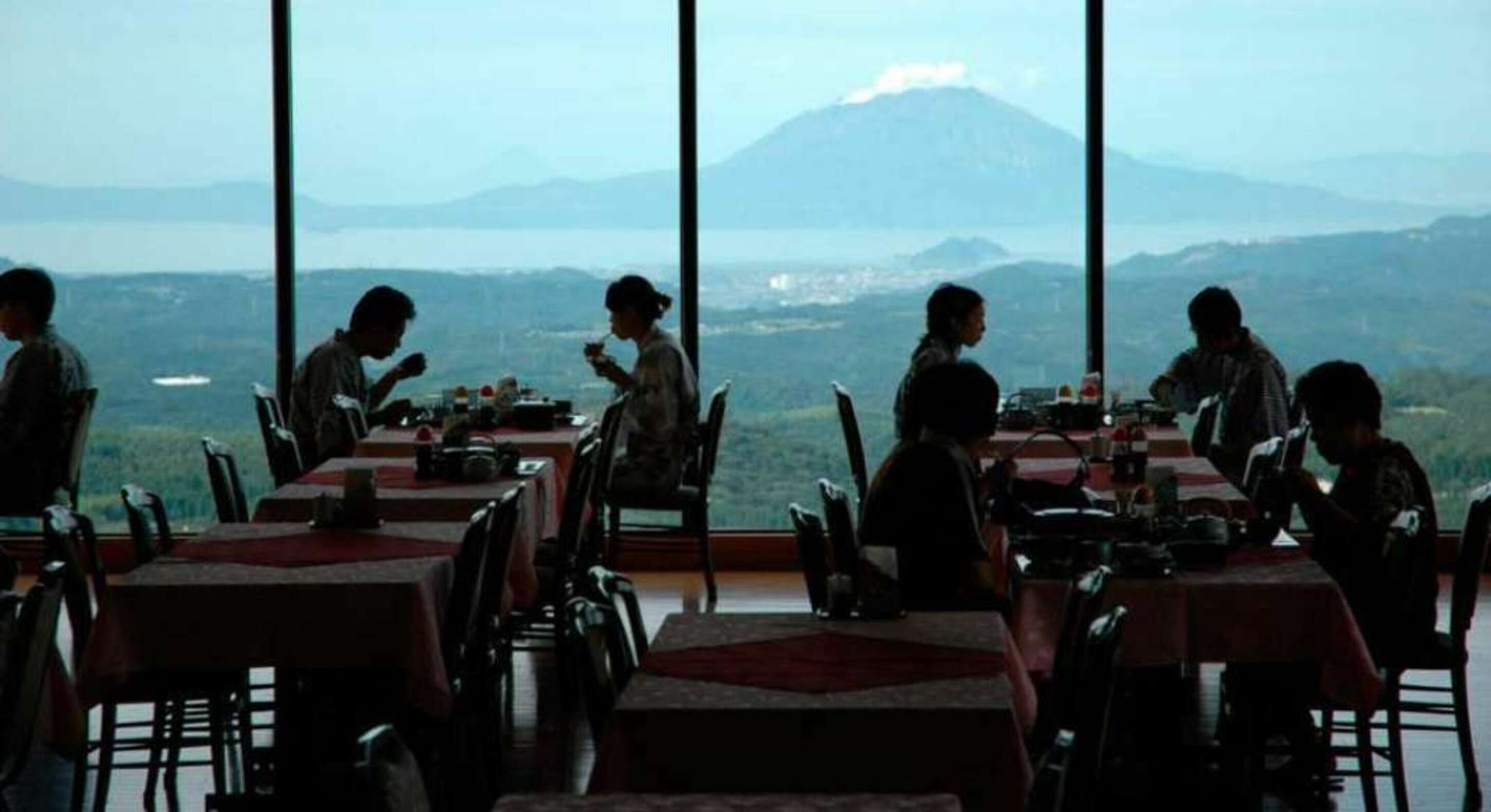 A restaurant with tables and chairs, large windows, and a view of a mountain and landscape.