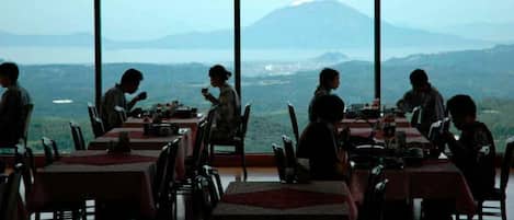 A restaurant with tables and chairs, large windows, and a view of a mountain and landscape.