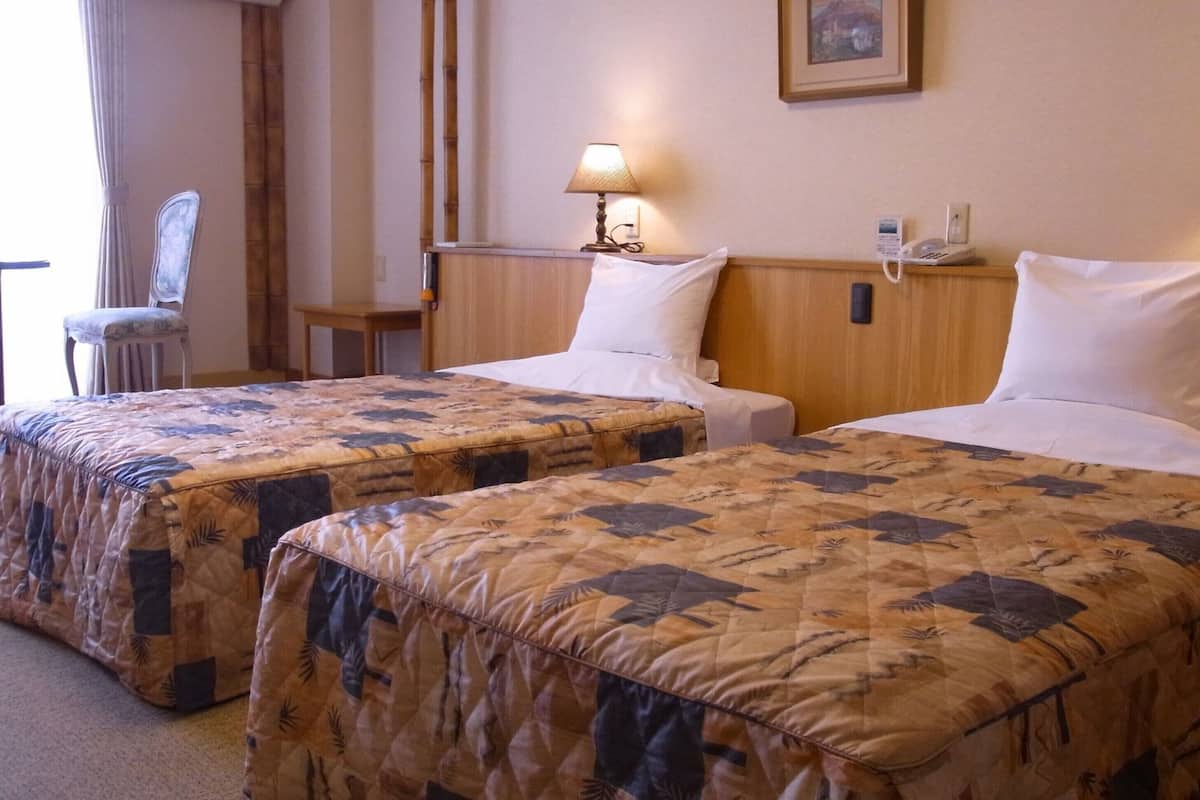 A hotel room with two beds, each with a patterned bedspread, bedside lamps, a chair, and a small table.
