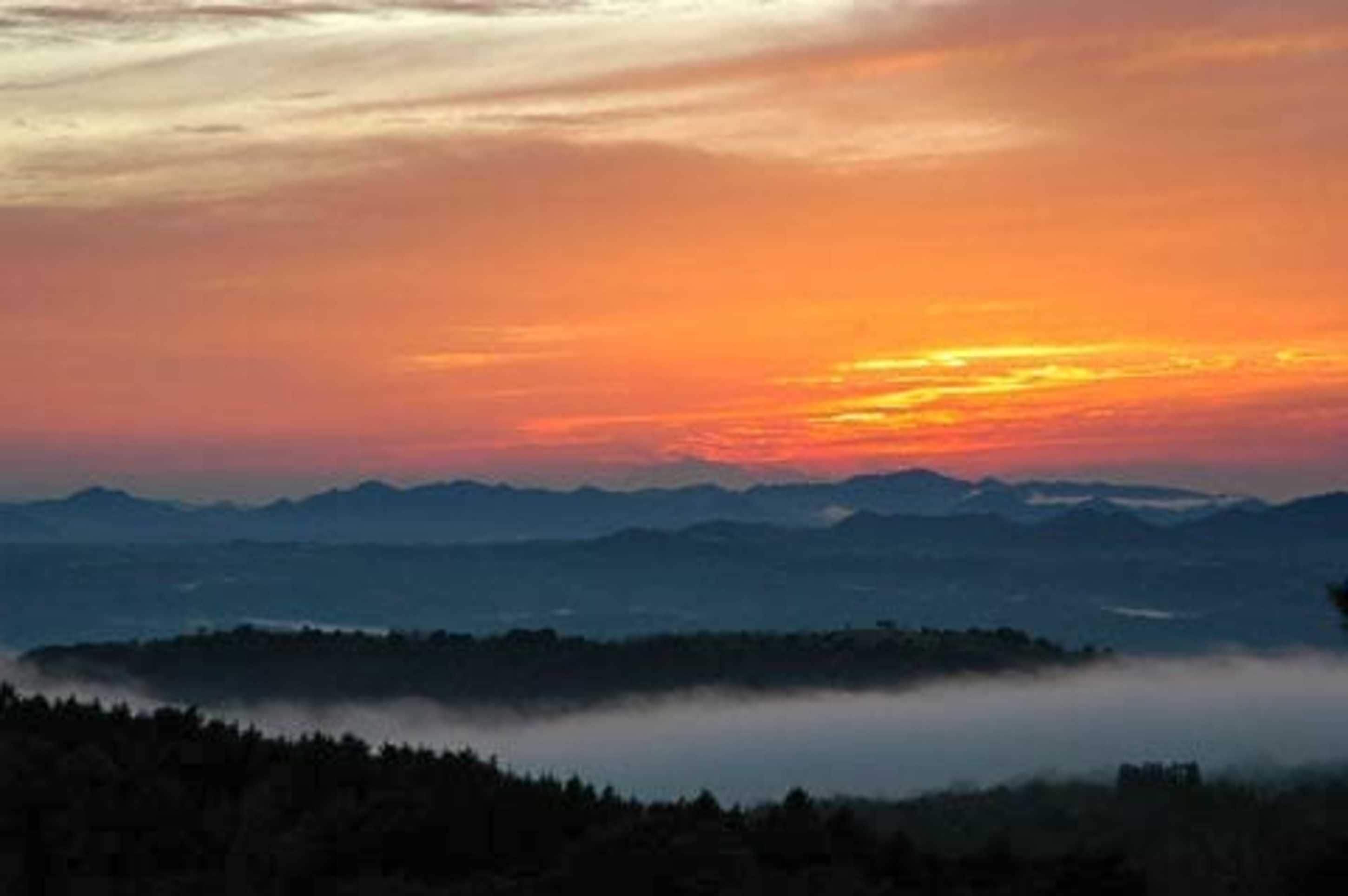 A mountainous landscape with a sunset and a layer of fog over the valley.