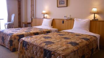 Quarto de hotel com duas camas de solteiro, cada uma com colcha estampada e travesseiros brancos. Há luminárias de cabeceira, um telefone e uma cadeira no quarto.