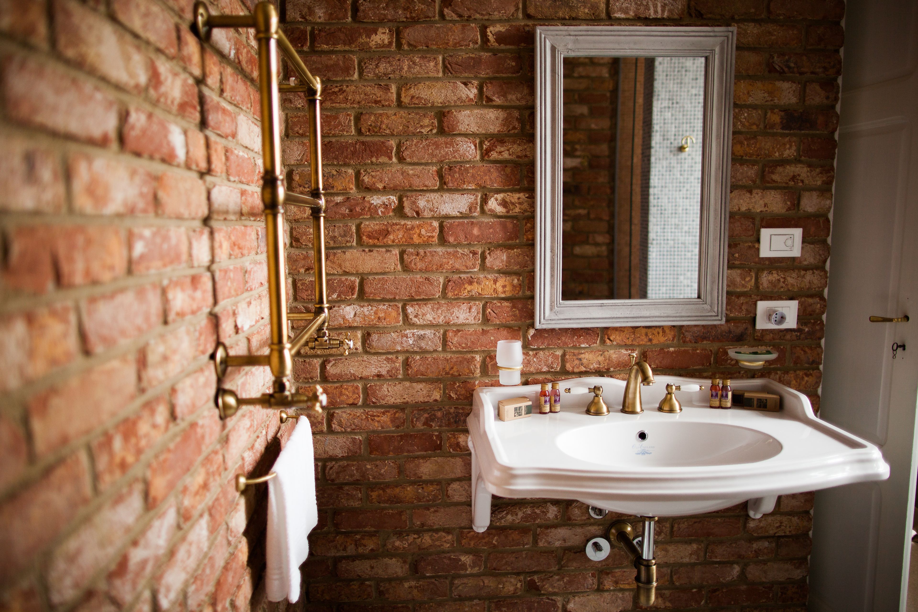 A bathroom with a white sink, gold fixtures, and a brick wall.