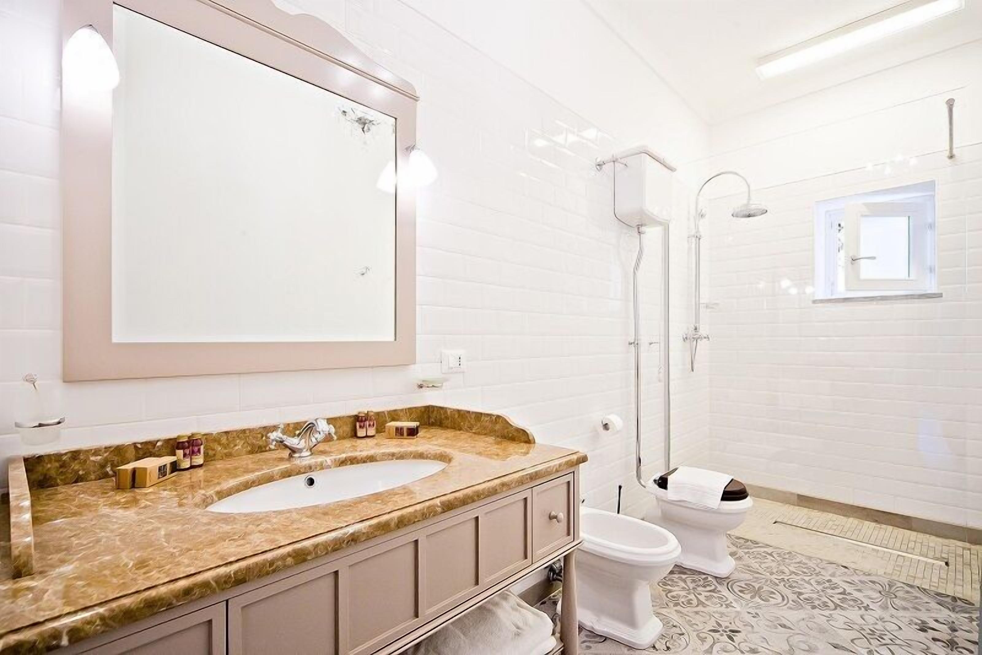 Un baño con un espejo grande, un lavamanos, dos inodoros y una ducha.